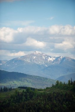 Bereketli yeşil tepeler, güzel bir günde açık mavi bir gökyüzünde süzülen kar örtülü zirveler ve kabarık bulutların yer aldığı önemli bir dağ sırasına çıkar..