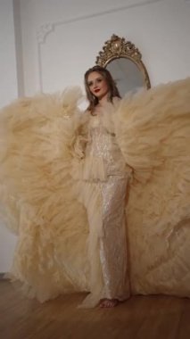 Eski bir aynanın arkasına dayanan uzun trenli lüks elbiseli bir kız treni fırlatıyor.