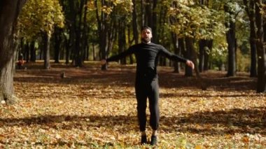 Genç bir sporcu, sarı sonbahar yapraklarıyla kaplı bir parkta boks antrenmanına hazırlanmak için egzersiz yapıyor ve vücudunu esnetiyor..