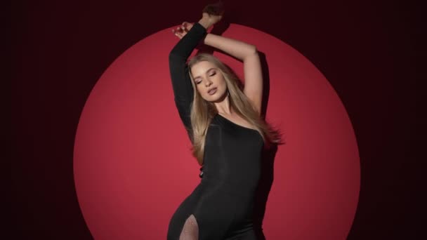 一个穿着紧身黑色连衣裙的性感女人在红色背景下反射着柔韧的身体 演播室里身材性感的美女时尚的视频 慢动作 — 图库视频影像