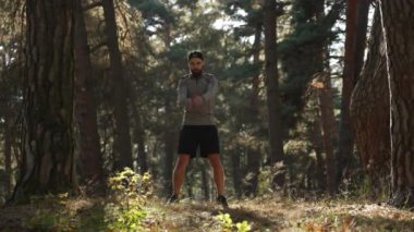 Bir adam kollarını ve omuzlarını yeşil ağaçların arkasına uzatıyor.