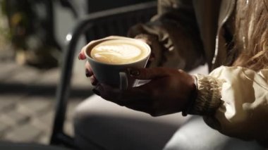 Güzel bir kız bankta otururken kahve içer. Kız dışarıda sıcak kahve içiyor. Güzel bir genç kadının portresi, yakın plan..