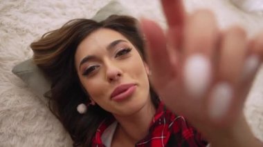 Baştan çıkarıcı kız yatağa uzanıyor ve telefonda video çekiyor.