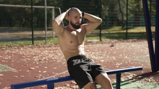 一个年轻人正在一个城市公园的室外运动场上锻炼 这家伙做体操 腹部肌肉训练 街头模拟器方面的培训 健康的生活方式 — 图库视频影像