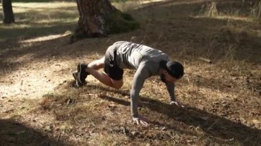 Genç adam karın kaslarını şişiriyor. Adam ellerinin üzerinde duruyor ve leğen kemiğini büküyor ve karın kasları üzerinde egzersiz yapıyor. Açık hava sporları.