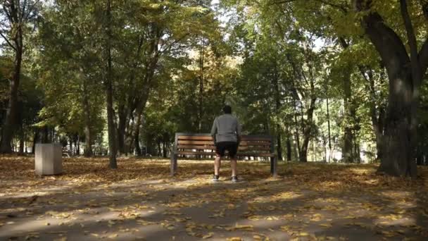 在秋天的公园里 肌肉运动员在长椅上跳着做腿部运动 后视镜 — 图库视频影像
