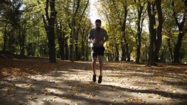 İyi bir atletik vücudu olan genç bir adam sonbahar parkında atlarken kardiyo antrenmanı yapıyor.