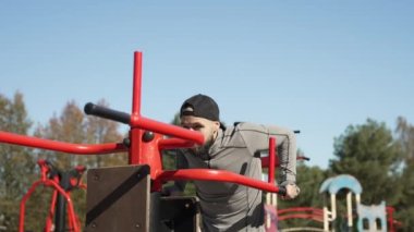 Genç bir adam dışarıda egzersiz makinesinde kol kaslarını esnetir.
