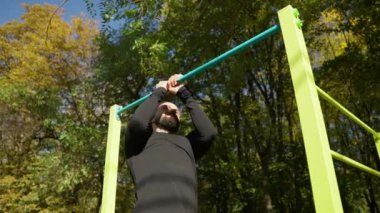 Yakışıklı genç vücut geliştirici, sonbaharda spor sahasında parkın yatay çubuğunda barfiks çekerek vücudunu geliştirir.