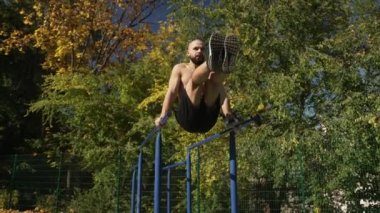 Spor sahasında yatay barda karın kaslarını pompalayan kaslı bir adam.