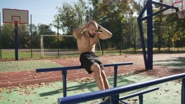 Mükemmel ve hafif vücutlu karizmatik genç adam kaslarına odaklanmış, spor sahasında güzel karın kaslarına sahip olmak için bacaklarını pompalıyor.