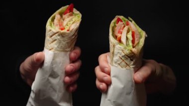 İnsanlar ellerinde sulu sebzeler ve ince pide ekmeğine sarılmış tavuk parçalarıyla iki shawarma tutuyor. Ulusal Mutfak Restoranı. yavaş çekim