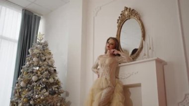 Güzel bir genç kız, süslü bir Noel ağacına hayranlıkla bakar. Şenlik salonunda.