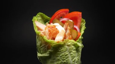 Marul yapraklarına sarılı nefis bir shawarma, siyah bir arka planda.