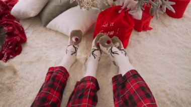 İki aşık odada oturmuş, üzerinde geyik resmi olan çoraplar giyiyorlar. Sıcak bir dairede çorap içinde bir çift ayak, Noel sabahı uyanmak.