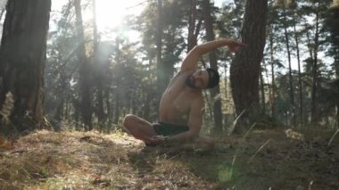 Genç sakallı bir adamın portresi. Orman ağaçları arasında oturmuş, rahatlıyor, temiz hava soluyor, gözleri kapanıyor. Erkek, parkta sakin ve huzurlu bir hayatın tadını çıkarıyor. Açık havada..