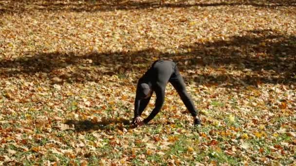 男性は筋肉を伸ばす練習をし 側面に傾いている 秋のアウトドア — ストック動画