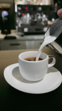 Bir adam beyaz bir fincanda kahveye süt döker..