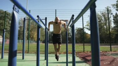 Çıplak gövdeli sakallı bir adam spor sahasında yatay bir çubuğa tırmanıyor. Sporcu figürü. Kolların ve sırtın kaslarını salla.