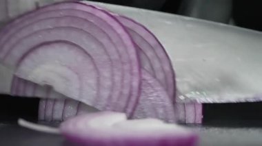 Bir evin ya da restoranın mutfağında yemek pişirmek. Kesme tahtasındaki şef pembe soğanı bıçakla yemek için dilimlere ayırıyor. Lezzetli bir öğle yemeği için malzemeler hazırlanıyor.