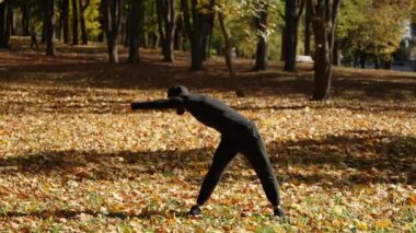 Sakallı ve spor üniformalı atletik beyaz adam sarı sonbahar ağaçları arasında vücut kaslarını esnetiyor.