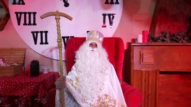 優しい陽気なサンタクロースが椅子に座って カメラを見て笑っています 聖ニコラスの肖像 クリスマスのための白い髭 — ストック動画