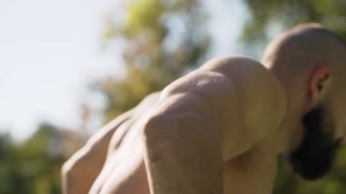 Bodybuilder quickly shakes his arm muscles on the exercise machine on the street. A man pulls his hands up to increase muscle mass. Man carries out the process of construction and development