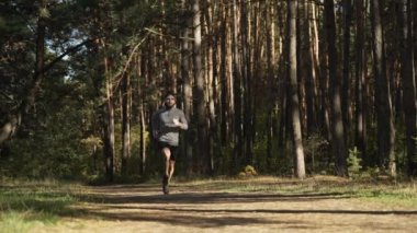 A man in sports clothes and a cap runs along a path through a dense pine forest. Healthy lifestyle, Cardio training