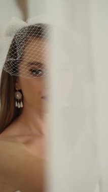An attractive naked girl is standing by the window with a veil covering her eyes
