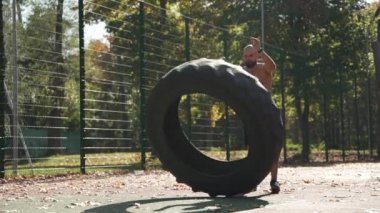 A young sports man does sports lifting a wheel on the sports ground