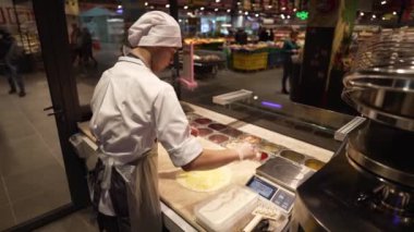 The cook prepares a delicious pizza and rubs hard cheese on the rolled dough and lays out pieces of bacon
