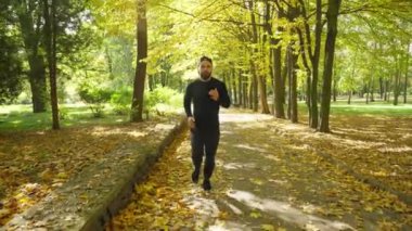 A young sportsman runs backwards in the park in autumn