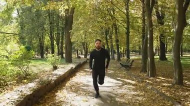 Attractive man jogging in the park against the background of trees. Cardio training in nature