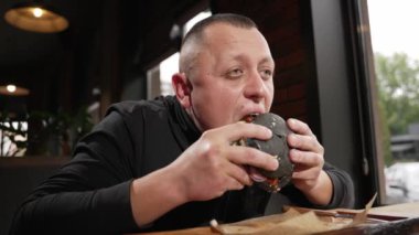 A man sits at a table in a pub and eats a burger