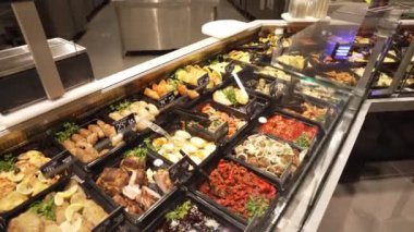 A variety of fried foods in trays are laid out in the store. Salads and ready-made meat products