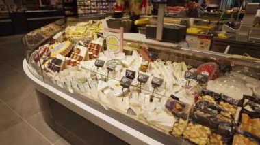 Cheese on the shelf in the supermarket. Horizontal panning. A large selection of colorful cheeses.