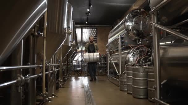 一位男性酿酒师穿过一个酿造工艺啤酒的车间 手里拿着一大桶令人陶醉的饮料 — 图库视频影像