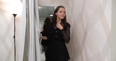 The girl leaves the fitting room and looks in the mirror