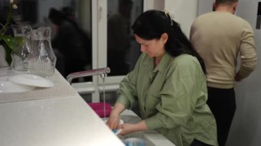 A woman washes the dishes, and a man helps her with housework