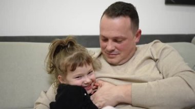 A father hugs his little daughter while sitting on the sofa at home