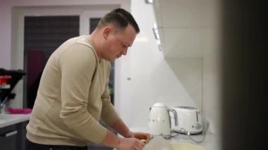 Man preparing healthy vegan food alone at home, smiling, cutting fresh vegetable salad while standing in modern kitchen interior