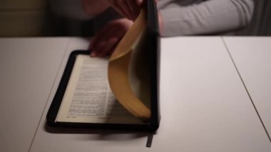 A man opens the Bible and reads prayers while sitting at the table at home