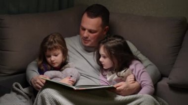 A loving father reads an interesting bedtime story to his preschool children. Concept of parenthood, love and happy family.