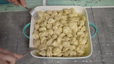 People take dumplings from a plate by stabbing them with a fork. View from above