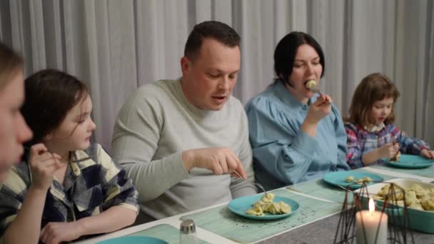 お母さんとお父さんと子供たちは一緒にテーブルに座っておいしい食べ物を食べる — ストック動画