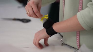 A womans hand removes a pin from a backing attached to her hand and attaches patterns to fabric