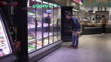 A man chooses products in a supermarket, looks at the window and reads the labels