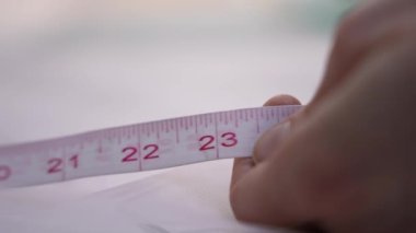 A seamstress takes a tape measure and measures it in feet, inches, and centimeters.