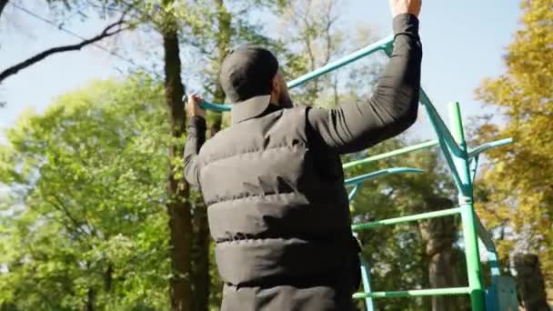 Bir Adam Sonbahar Parkında Yatay Bir Çubuğa Tırmanıyor — Stok video