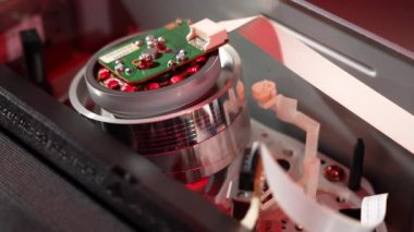 A cassette is inserted into the VCR and the video from inside is played. Up close the film is pulled onto the reel